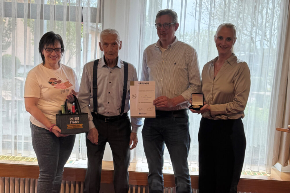 Ein Gruppenfoto mit zwei Männern und zwei Frauen. Ein Mann hält eine Urkunde in der Hand, die Frau rechts hält eine goldene Medaille in der Hand
