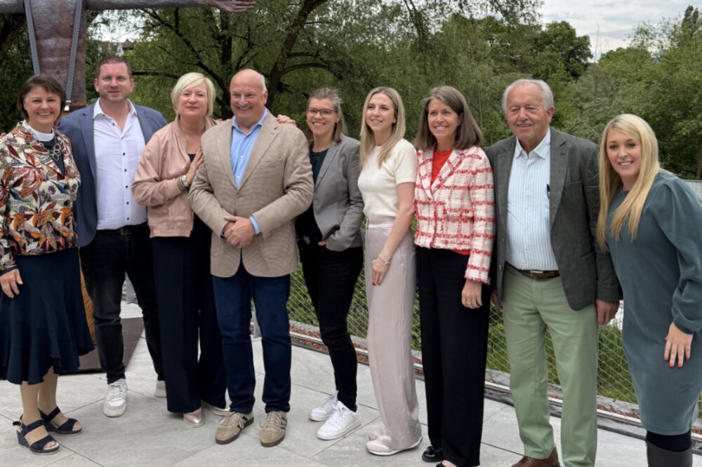 Sechs Frauen und drei Männer posieren im Freien für ein Gruppenfoto. Sie lächeln.