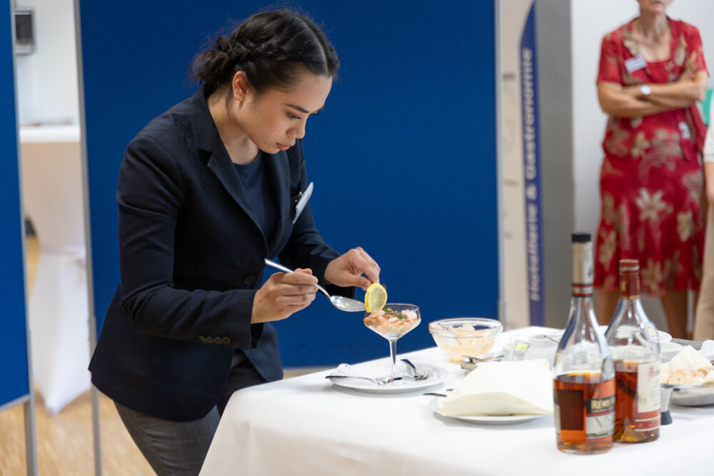 Eine junge Frau in Berufskleidung des Gastgewerbes serviert einen Cocktail