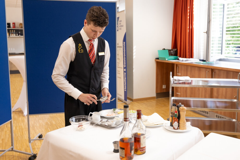 Ein junger Mann in der Berufskleidung des Gastgewerbes räumt einen Tisch ab