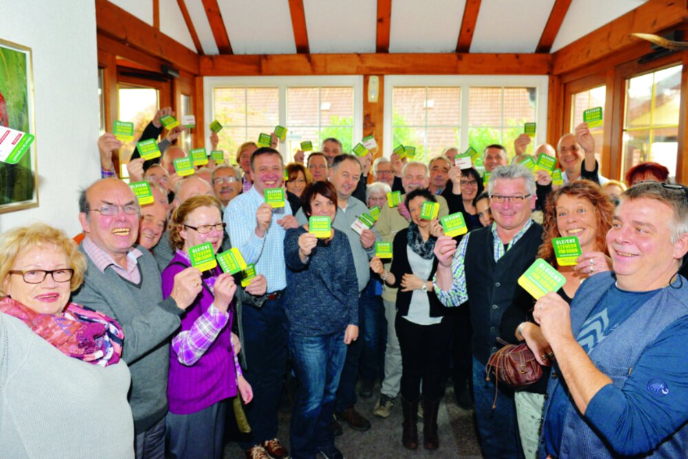 Foto vieler Menschen in einem Haus. Alle halten grün-gelbe Bierdeckel in den Händen.