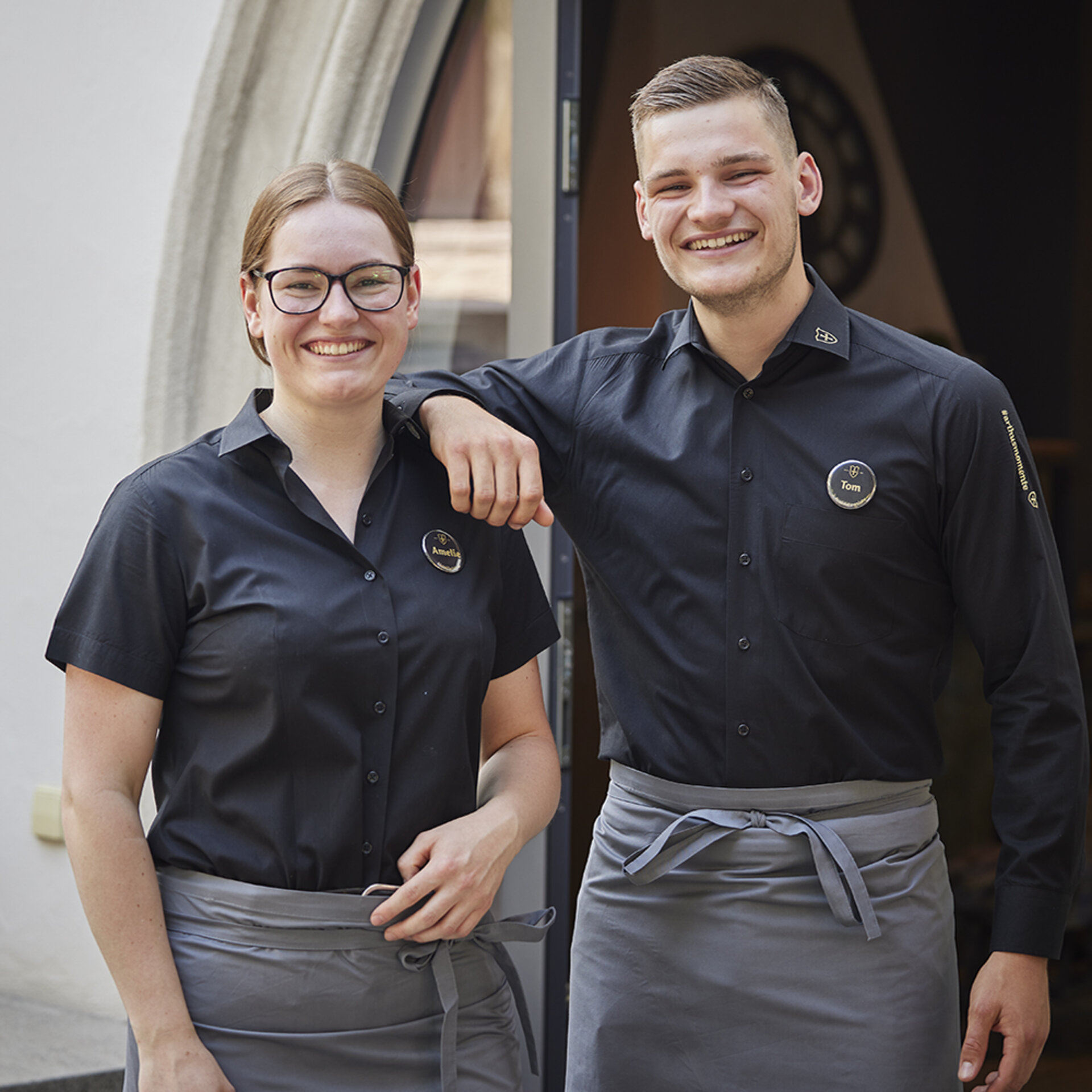 Abbildung von zwei Auszubildenden in Arbeitskleidung, die freundlich in die Kamera lächeln