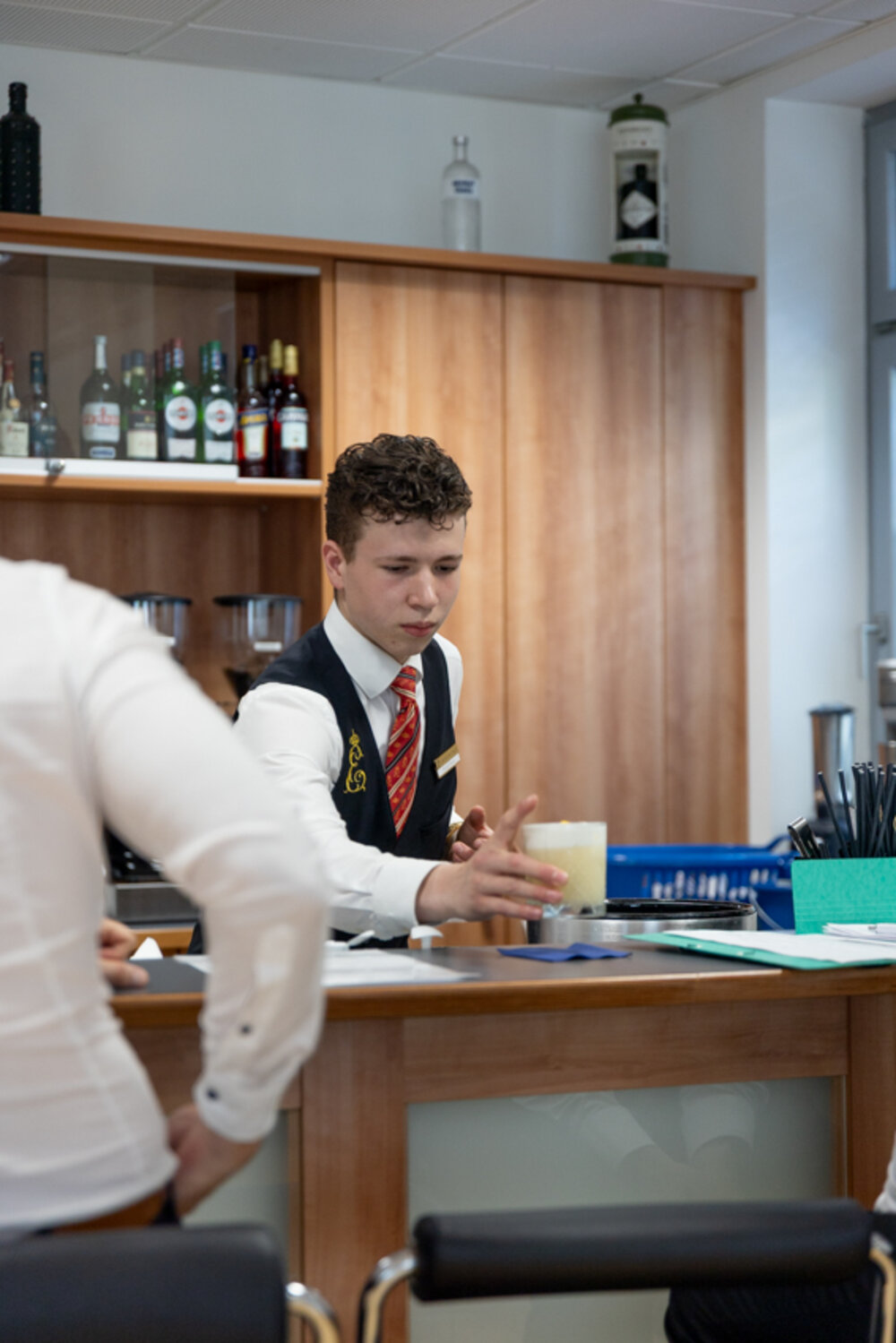 Ein junger Mann in Berufskleidung des Gastgewerbes stellt einen Cocktail auf eine Bar