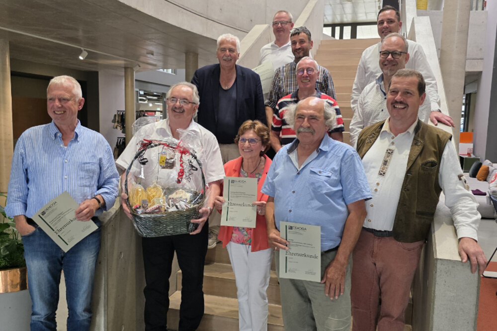Ein Gruppenfoto mit mehreren Menschen vor bzw. auf einer Treppe. Zum Teil halten die Personen Urkunden in den Händen. Alle lächeln