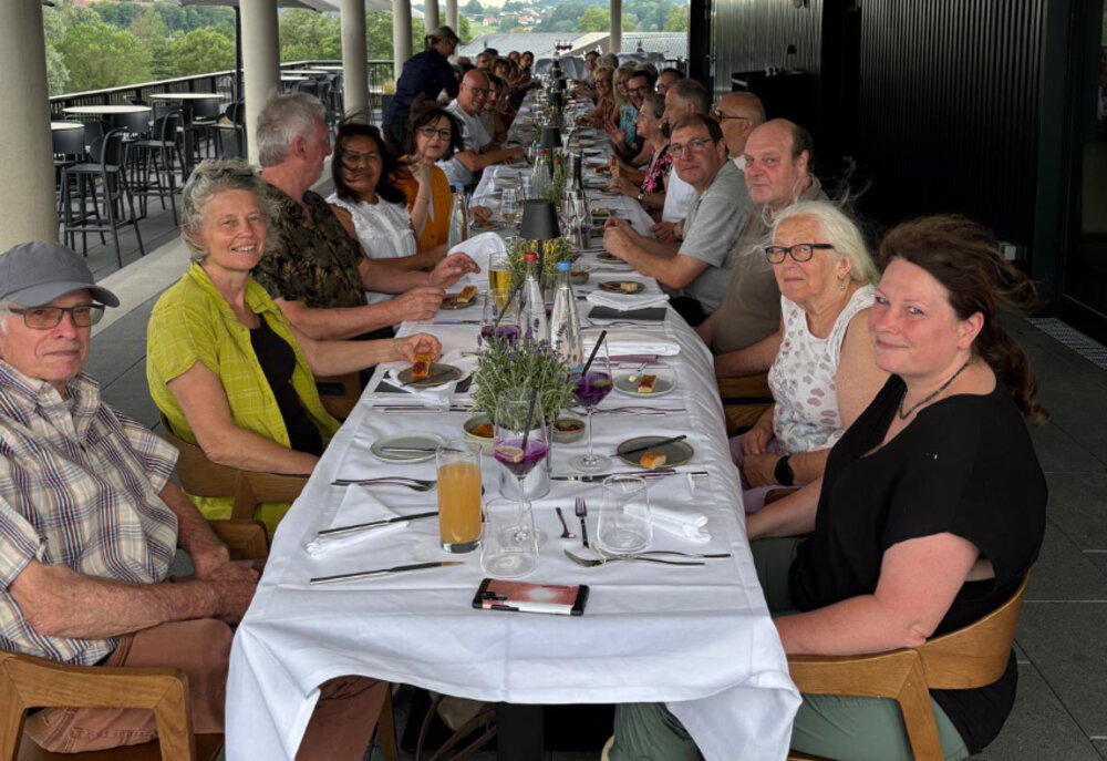 Eine lange Tafel, an der viele lächelnde Menschen sitzen und sich unterhalten