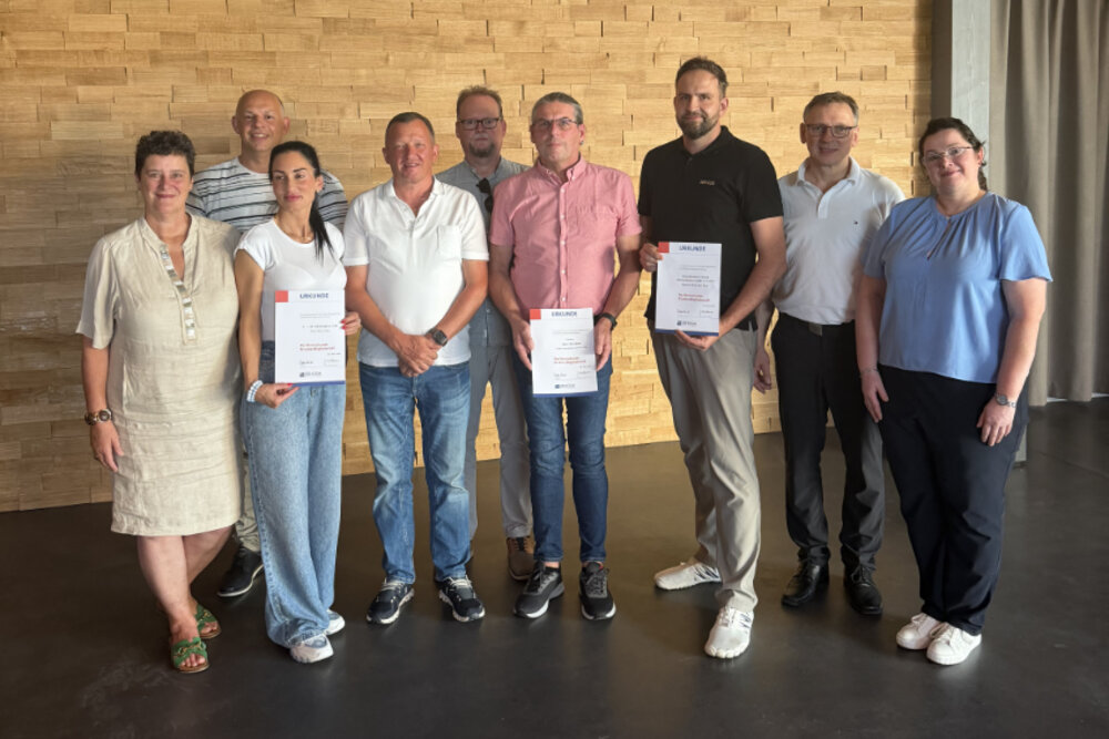 Neun Personen posieren für ein Gruppenfoto. Drei von ihnen haben je eine Urkunde in der Hand