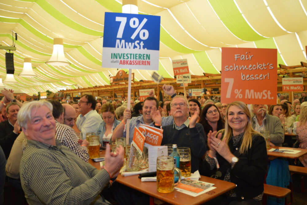 Foto vieler Menschen in einem Festzelt. Sie halten Demonstrations-Schilder pro 7 % in den Händen.