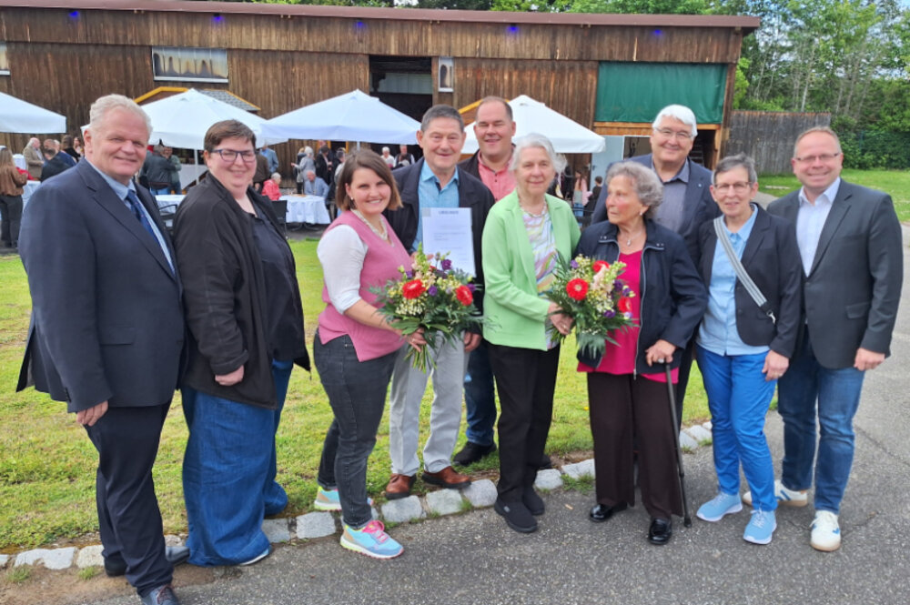 Zehn Menschen posieren lächelnd für ein Gruppenfoto im Freien.