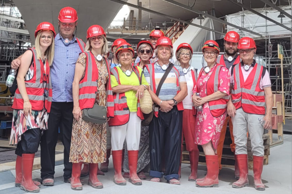 Eine Gruppe posiert für ein Foto auf einer Baustelle - alle tragen rote Warnwesten und Schutzhelme