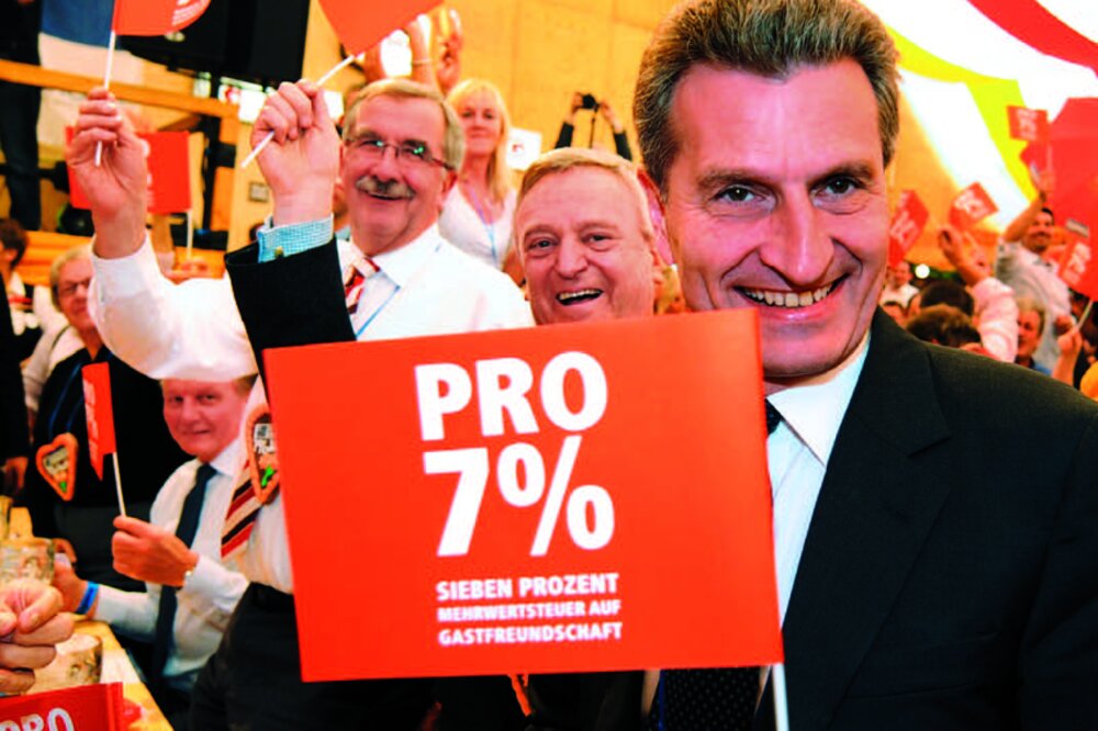 Foto eines Mannes mit einem 7%-Fähnchen in der Hand. Im Hintergrund viele Menschen in einem Festzelt.