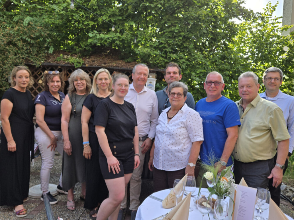 Gruppenfoto mehrerer Menschen im Freien. Im Vordergrund ein gedeckter Tisch