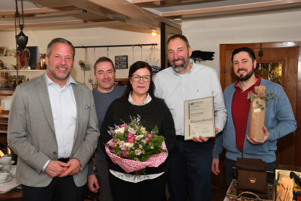Fünf Menschen posieren für ein Gruppenfoto, eine Frau hat einen Blumenstrauß in der Hand.