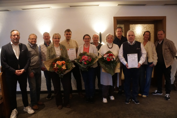 Viele Menschen posieren für ein Gruppenfoto, manche mit Blumensträußen und Urkunden in der Hand.