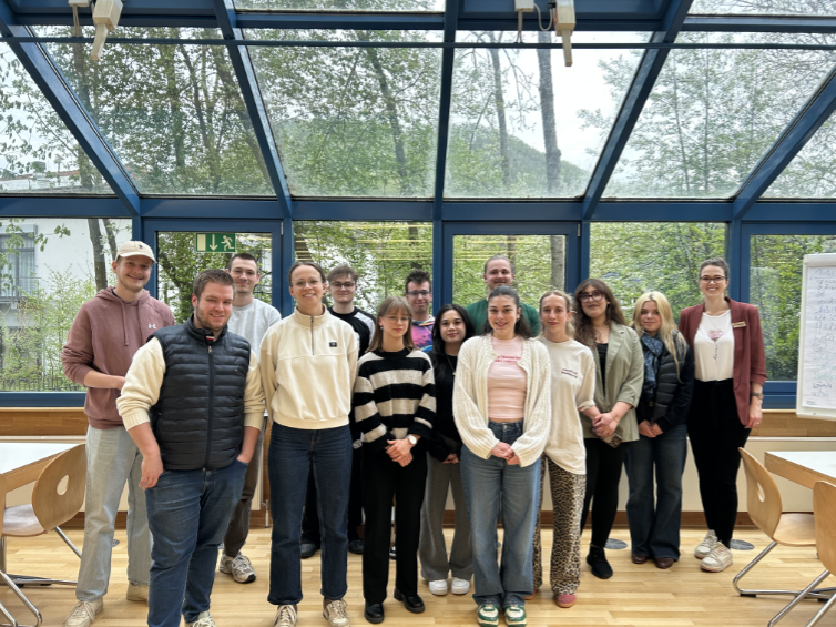 Eine Gruppe junger Menschen steht in einem Klassenzimmer vor einer Fensterfront.