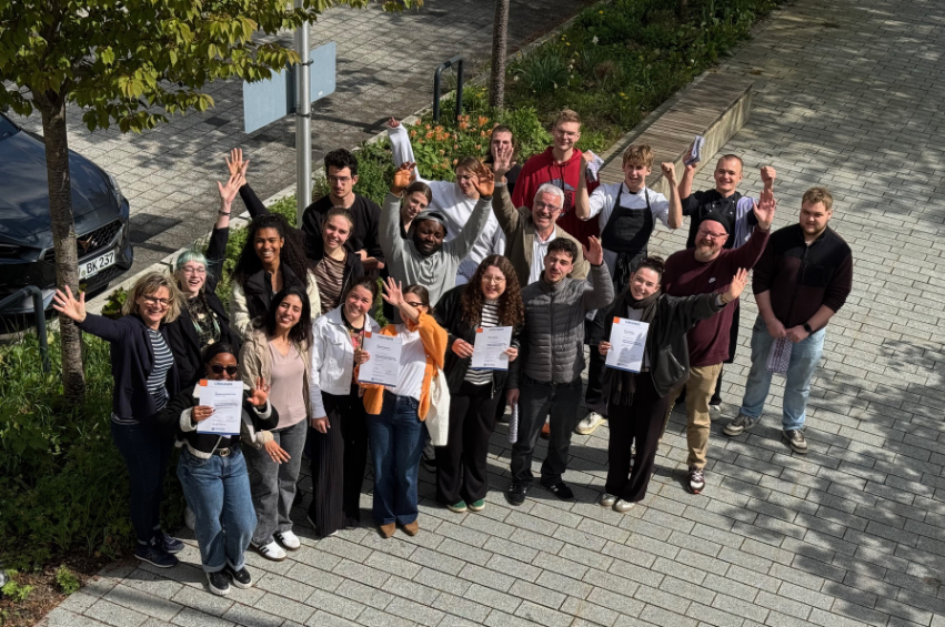 Eine Gruppe junger Menschen steht draußen im Freien und jubelt - das Foto wurde von oben aufgenommen.